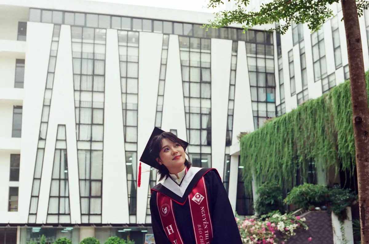 年轻女性身着毕业礼服,在户外现代建筑旁微笑留影。