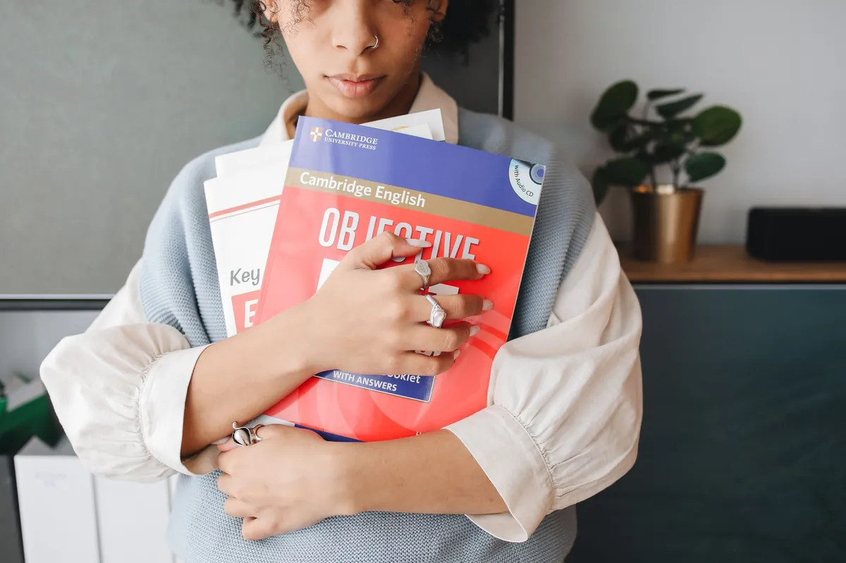 A young woman holding language study books indoors, symbolizing education and learning.